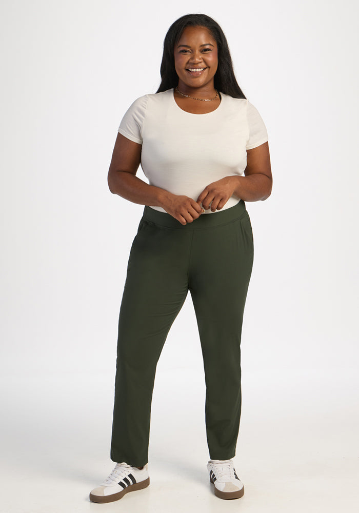 Woman smiles in Woolx Nicole Ankle Pants—Duffel Bag, styled with a white tee against a plain backdrop.