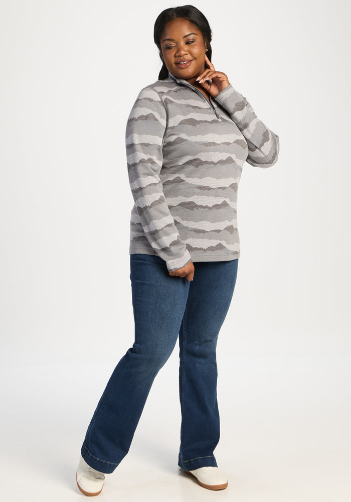 Woman in Woolx Emi 1/4 Zip - High Peaks pullover and blue jeans, smiling with one hand touching her chin.