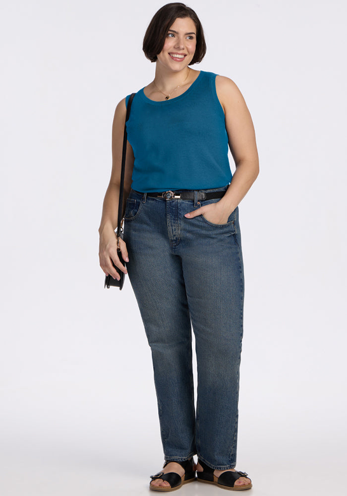 Woman in a Woolx Chessy Tank Top - Blue Pine, jeans, sandals, crossbody bag, standing and smiling at the camera.