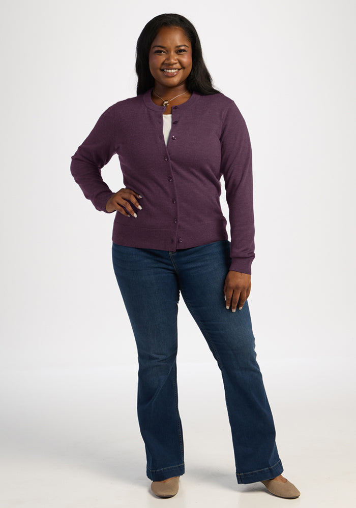 Woman smiling, wearing the Woolx Caitlin Sweater in Purple Iris with blue jeans and beige shoes against a white backdrop.