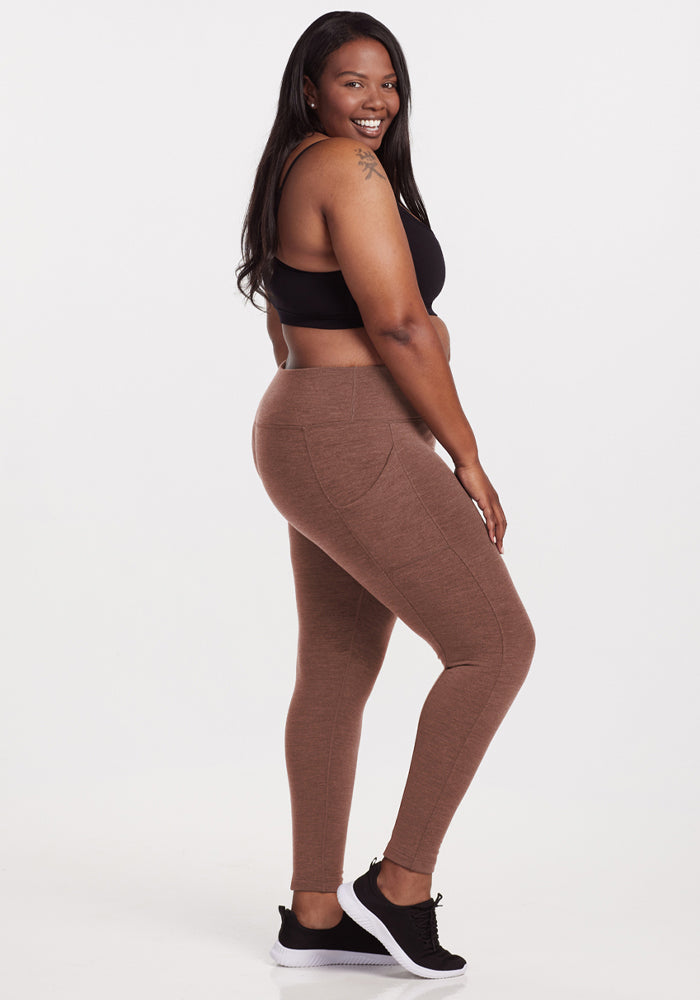 Woman in Woolx Piper Pocket Leggings - Sable Heather and black sports bra smiles, standing sideways on white.