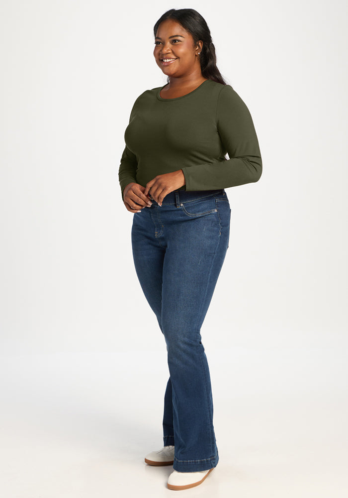 Woman in a Woolx Margot Bodysuit - Everleaf stands smiling against a white background, wearing blue jeans.