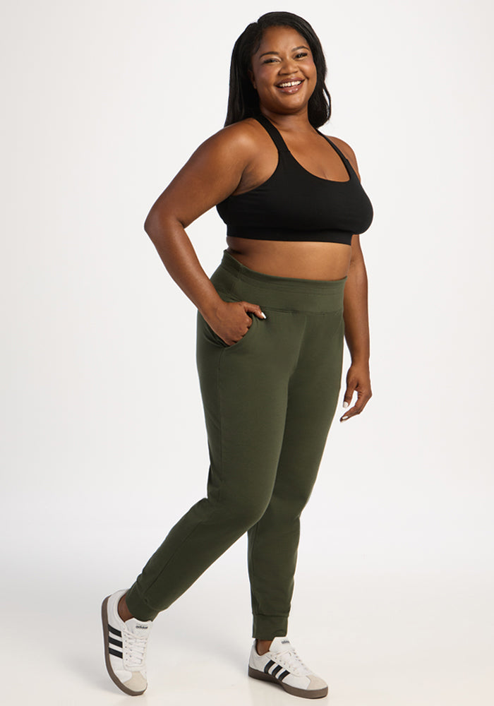 Smiling woman in a black sports bra and Woolx Madden Joggers - Everleaf poses against a plain white background.