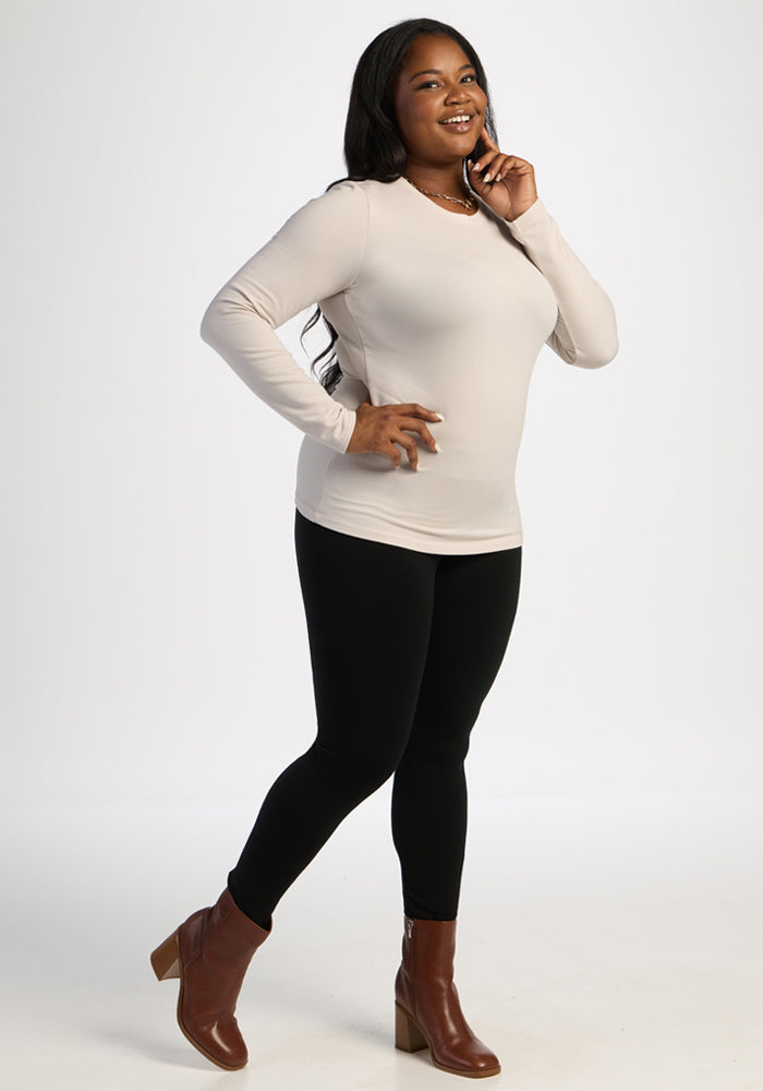 Woman in Woolx Sadie Baselayer Top - Ecru, black pants, brown heeled boots, standing against a white background.