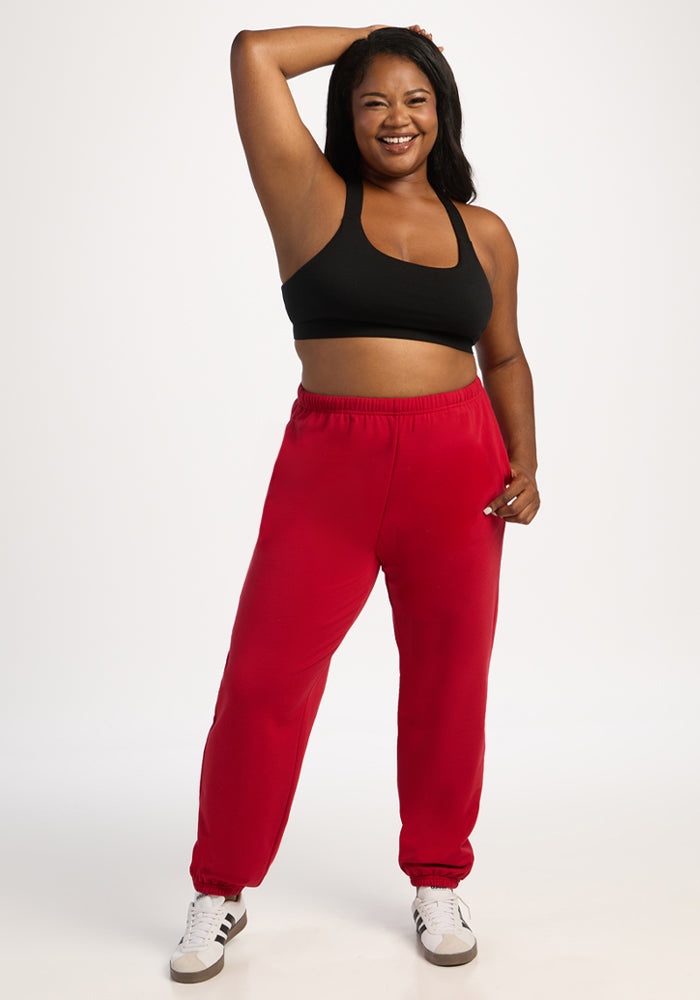 Smiling woman in Woolx Juliette Joggers - Maraschino Cherry, black sports bra, one arm raised, on white backdrop.