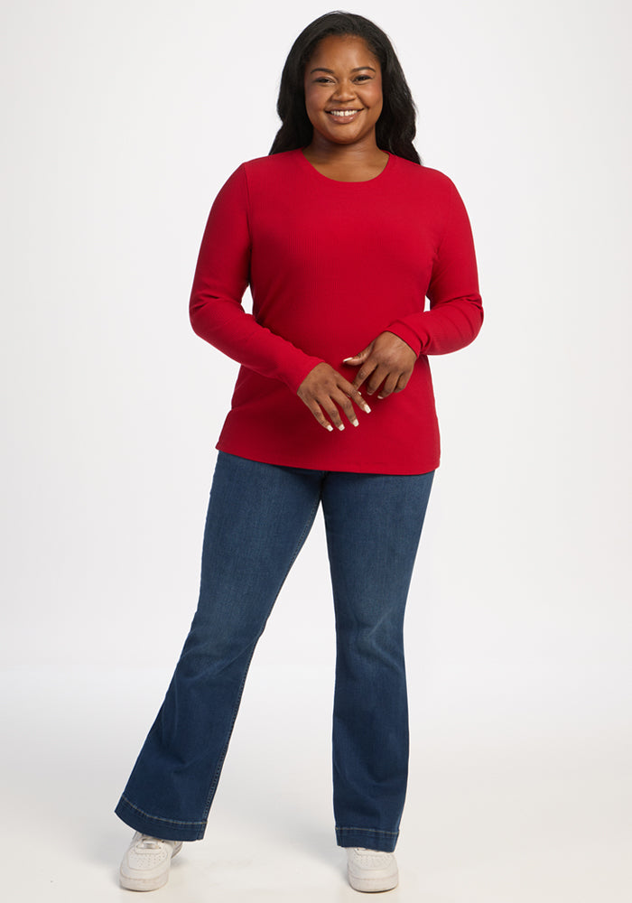 Woman smiles in the Woolx Hadley Ribbed Crew - Maraschino Cherry, blue jeans, and white sneakers by a white background.