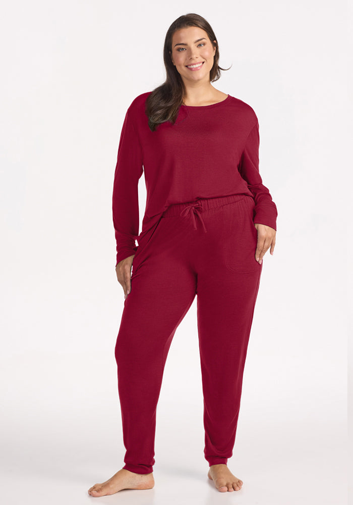 A woman wearing a matching long-sleeved shirt and deep red Woolx Mary Kate Lounge Pants in moisture-wicking Merino wool.