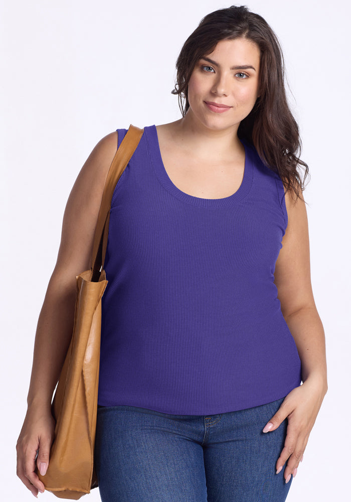 A woman in a Woolx Sloane Ribbed Tank - Berry Indigo and blue jeans holds a tan shoulder bag against a white background. 