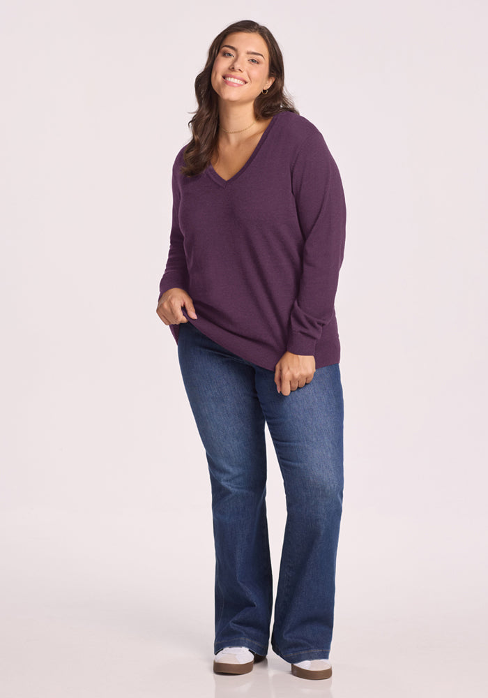 Woman in Woolx Francesca Sweater - Purple Iris and blue jeans smiles against a plain light background.