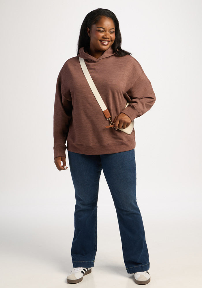 A woman in a Woolx Genevieve Hoodie - Sable Heather, blue jeans, and sneakers, with a crossbody bag.