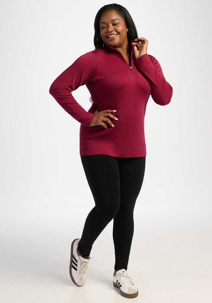 Woman in the Woolx Brooke 1/4 Zip - Beet Red smiles, posing in white sneakers and base layer leggings.