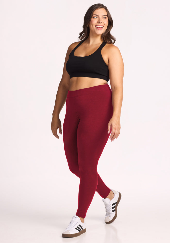 Woman in a black sports bra and Woolx Stella Leggings - Pinot Noir smiles while walking against a white background.