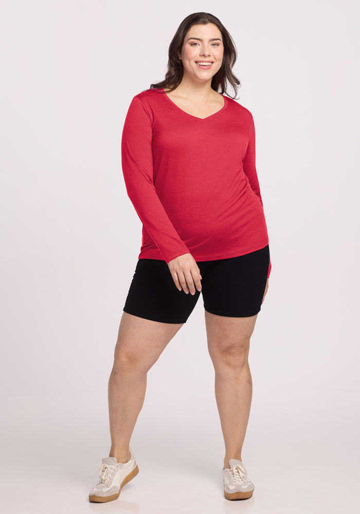 Woman smiling in a Woolx Millie Long Sleeve – Berry Ice Pop, black shorts, and white sneakers against a plain background.