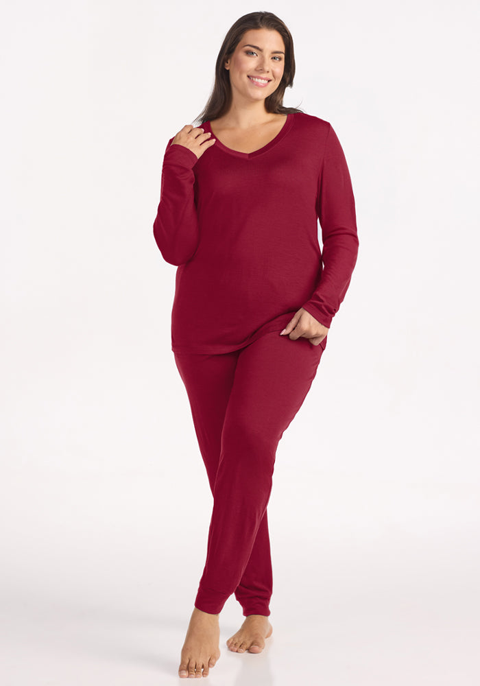 A woman wearing a beet red Lily V Neck Lounge Top and matching long-sleeved Merino wool lounge pants.