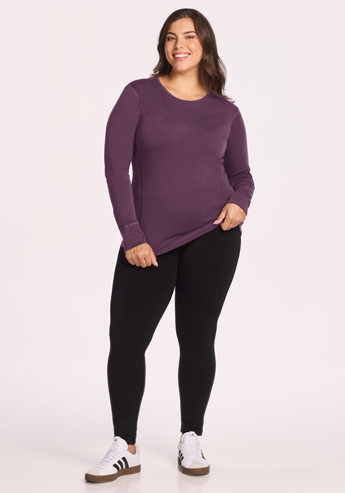 Woman in Woolx Hannah Long Sleeve Top - Purple Iris, black leggings, white sneakers, smiling at the camera.