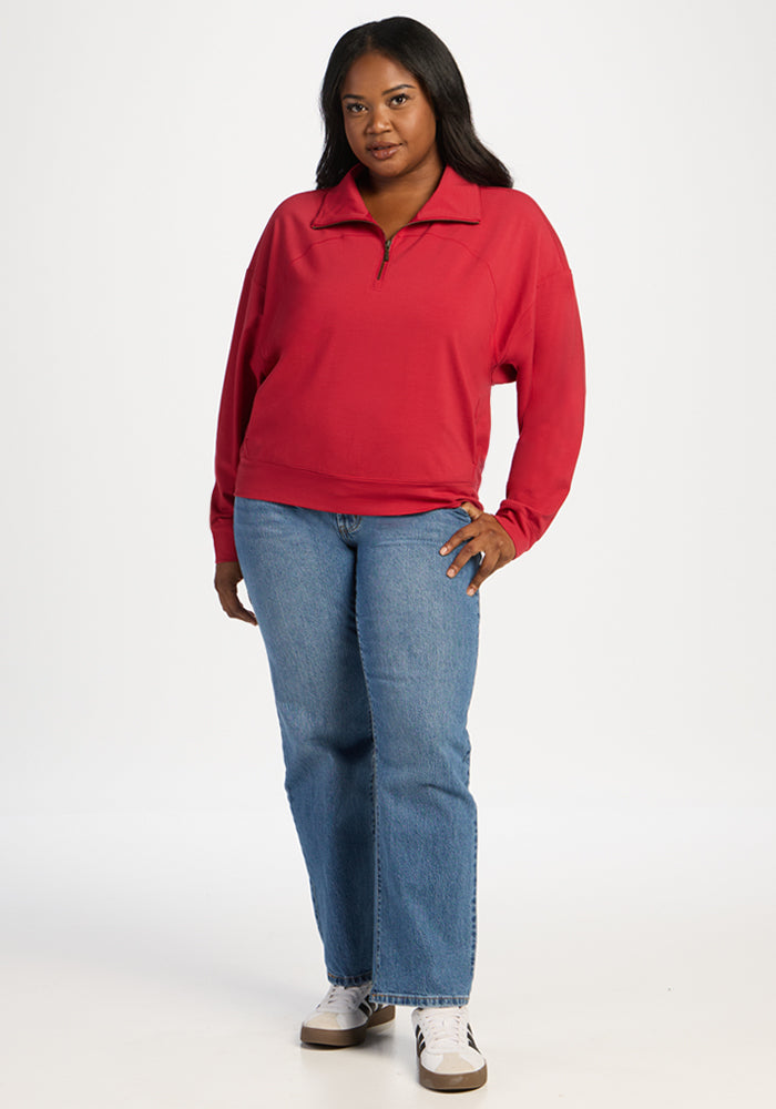 A woman wears a Maraschino Cherry Woolx Tori 1/4 Zip, blue jeans, and sneakers.