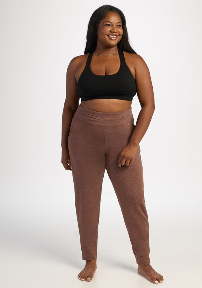 Barefoot woman in Woolx Willa Joggers - Sable Heather and a black sports bra stands against a white background.