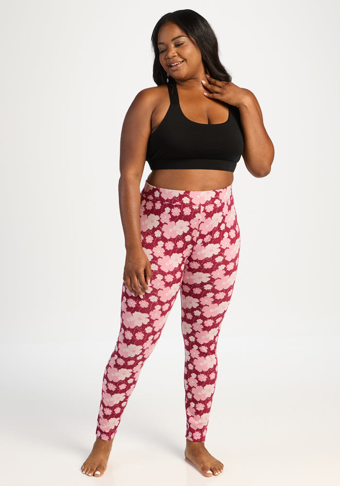 Barefoot woman smiles in a black sports bra and Woolx Taylor Baselayer Leggings - Floral Crush, hand on chest.
