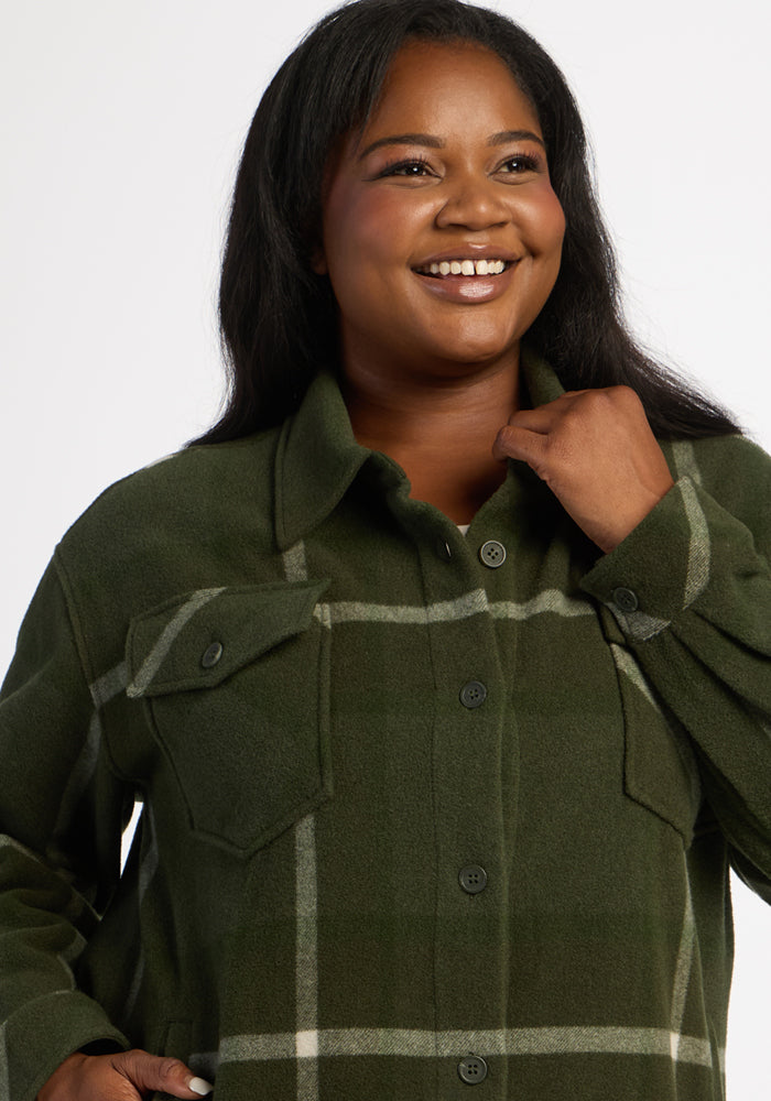 Smiling woman in the Woolx Sawyer Shacket—Driftwood Fern Plaid—with hand near collar, against a plain background.