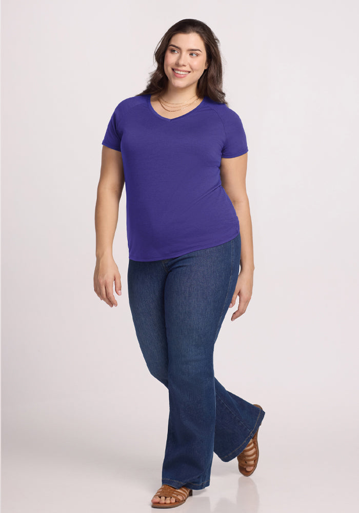 A woman in a Woolx Mia V Neck - Berry Indigo and blue jeans smiles against a plain white background.