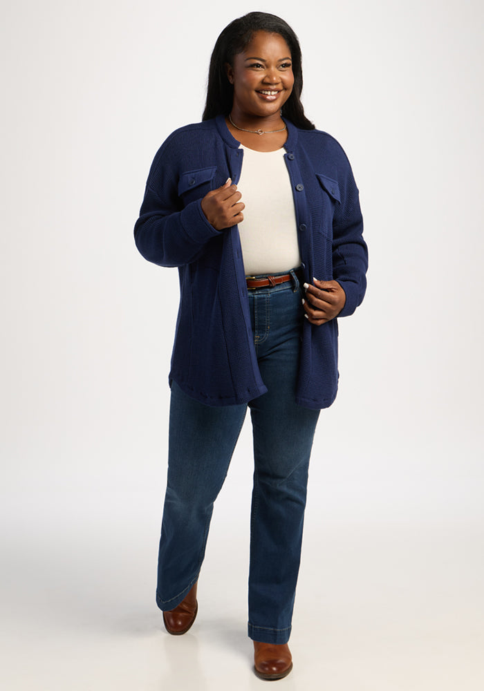 Woman smiling in Woolx Oaklynn Waffle Shacket - Ocean Cavern, white top, blue jeans, and brown shoes on white background.