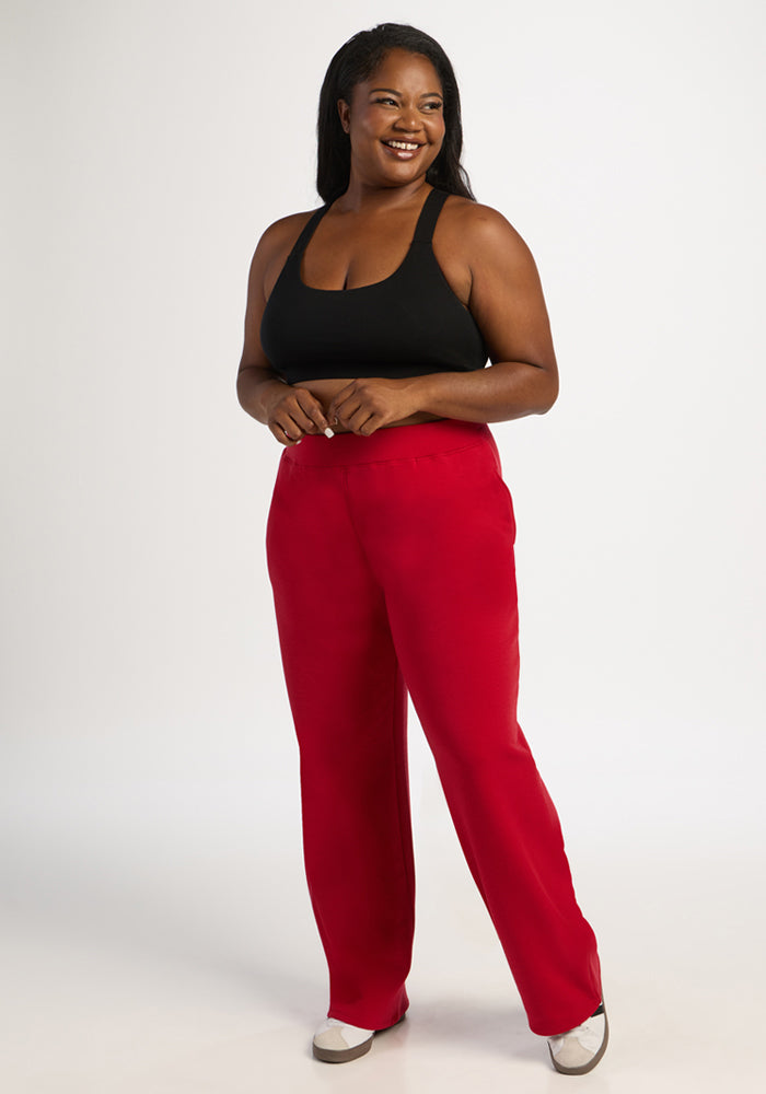 Woman in a black tank top and Woolx Bree Lounge Pants - Maraschino Cherry smiles, hands in pockets, on white background.