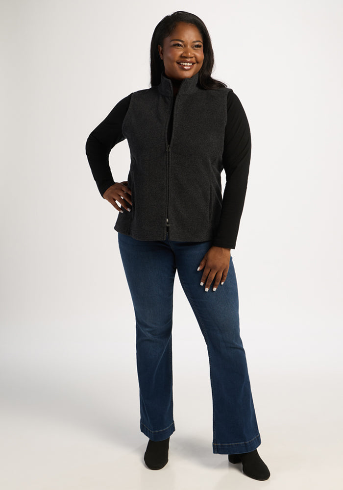 A woman smiles in the Woolx Haley Vest - Carbon Black, black top, blue jeans, and boots against a white background.