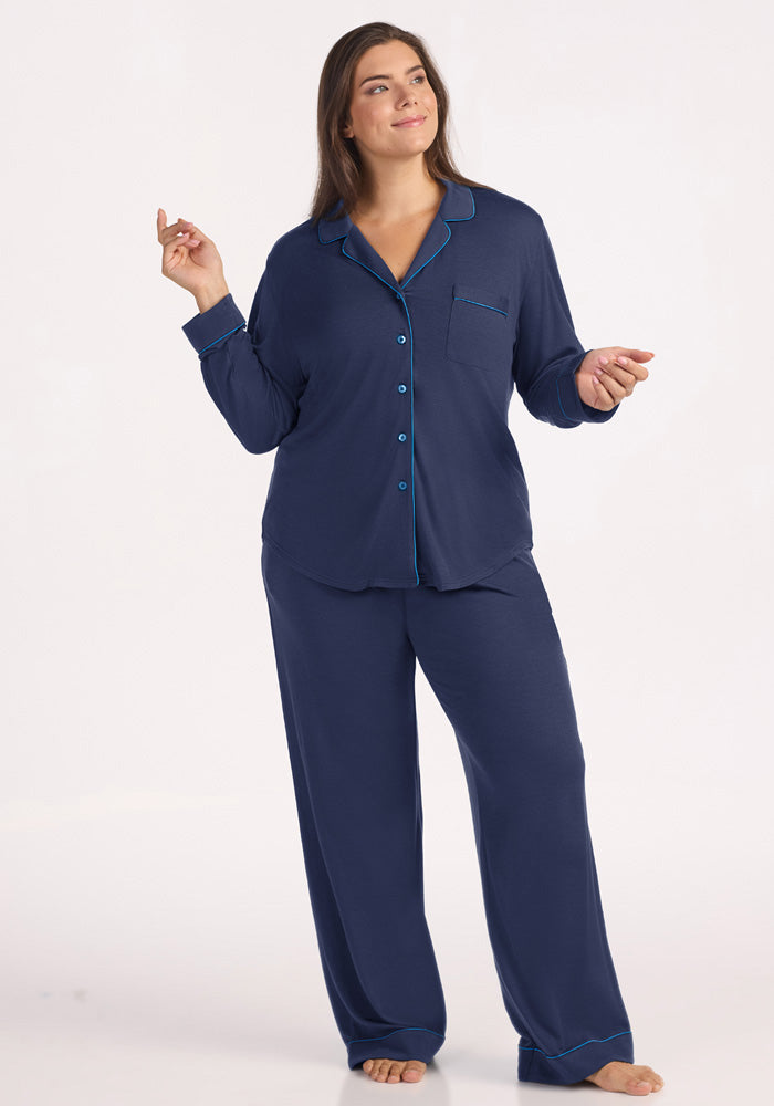 A woman wearing a dark blue Woolx Harper FeatherTouch® Pajama Set - Deep Dive with bright blue piping. 