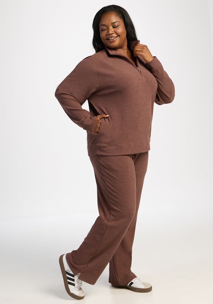 Woman in a Woolx Quinn Ribbed 1/4 Zip - Sable Heather and sneakers smiles with one hand in her pocket.