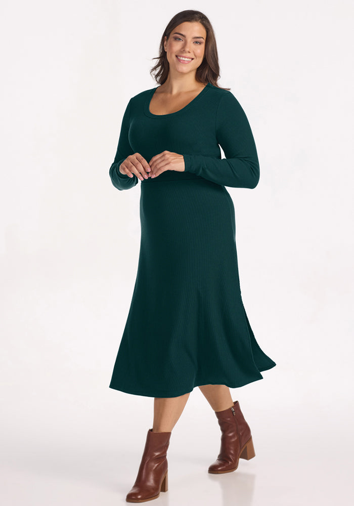 Woman in Woolx Caroline Ribbed Twirl Dress - Deep Pine, brown ankle boots, smiling against a white background.