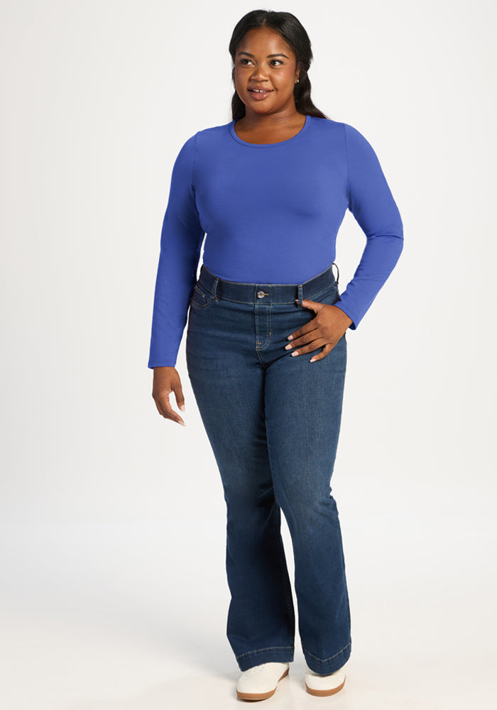 Woman wears Woolx Margot Bodysuit - Royal Blue and flared jeans, smiling against a plain white background.