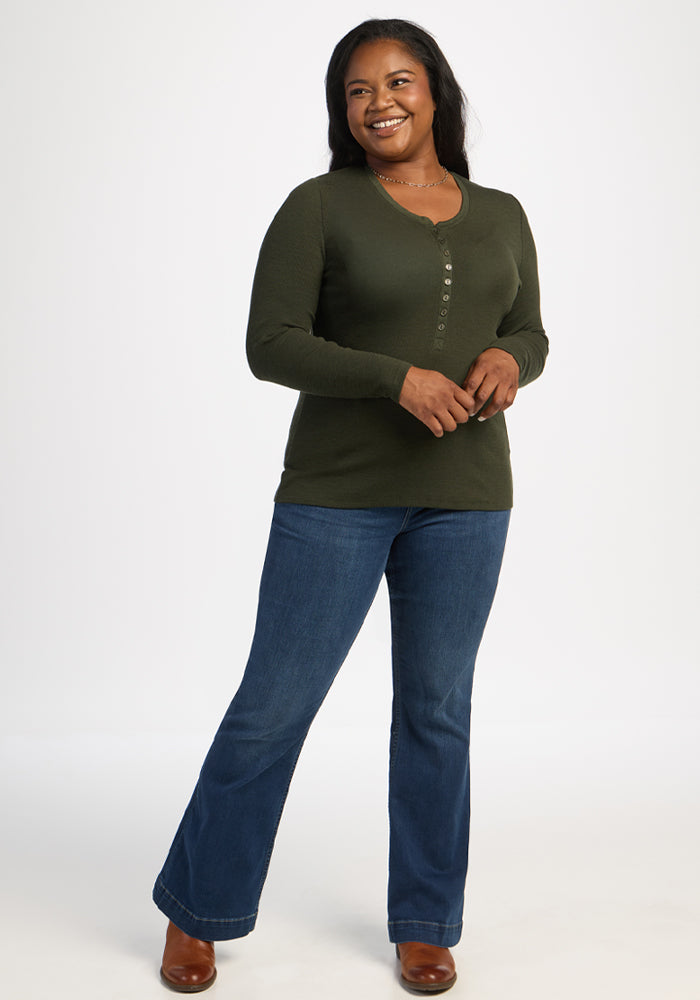 Smiling woman in a Woolx Reese Ribbed Henley - Duffel Bag and blue jeans stands against a white background.