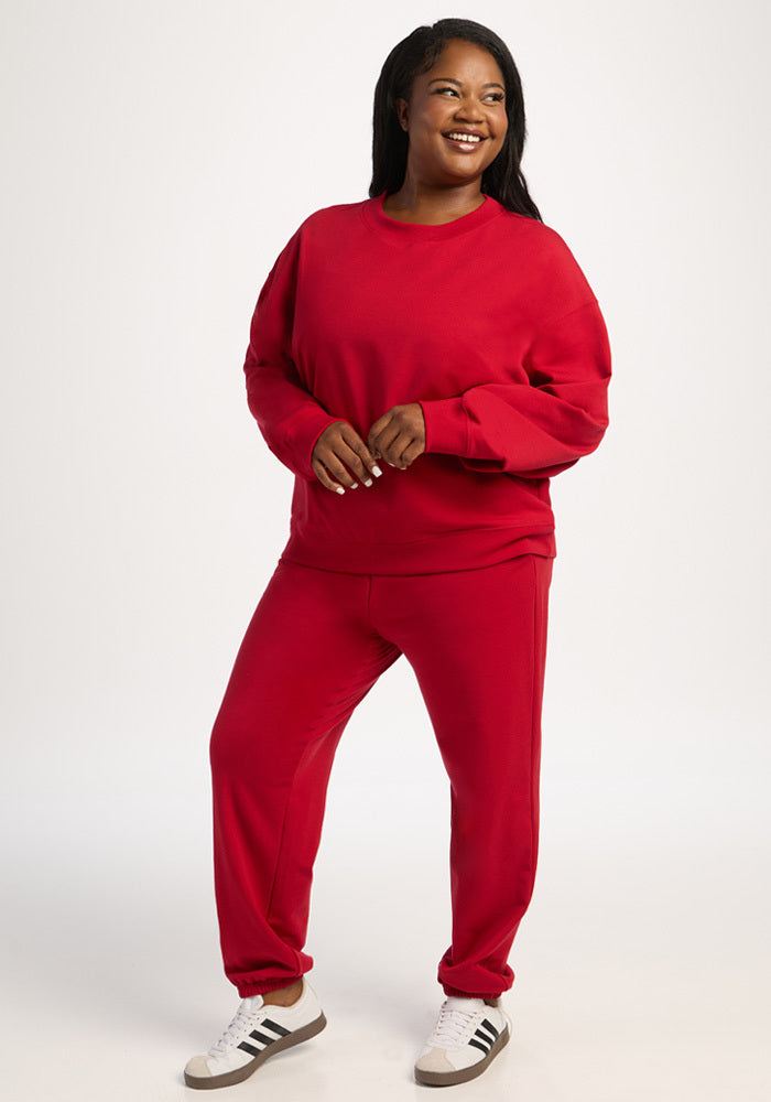 Smiling woman in a red Molly Crewneck - Maraschino Cherry sweatshirt, matching joggers, and white sneakers.