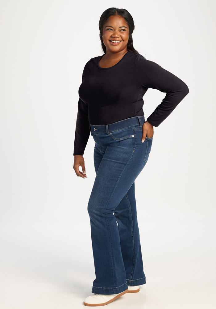 Woman in Woolx Margot Bodysuit—black, moisture-wicking—poses with one hand on her hip, wearing blue jeans.