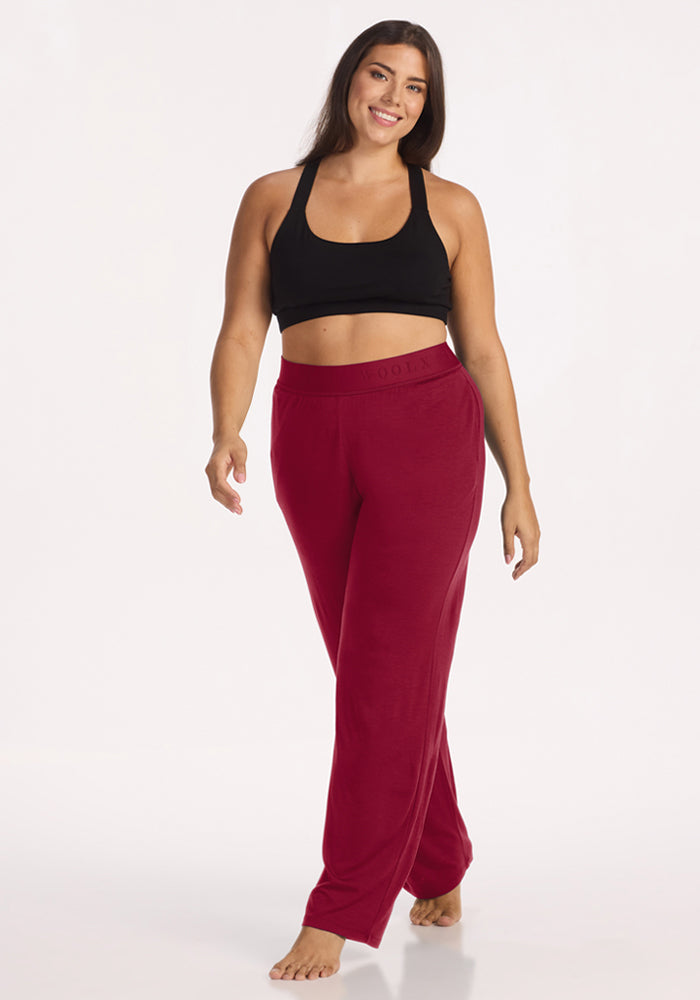 A woman wears a black sports bra and beet-red Maya Lounge Pants in a wide-leg style.