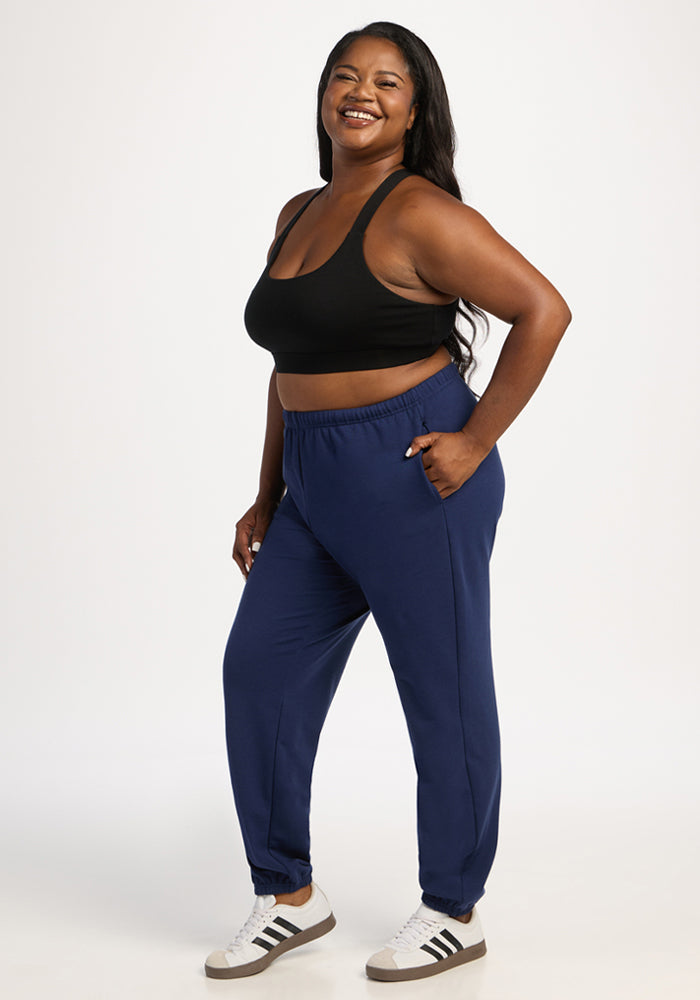 Woman in black sports bra and Woolx Juliette Joggers - Ocean Cavern stands smiling against a white background.