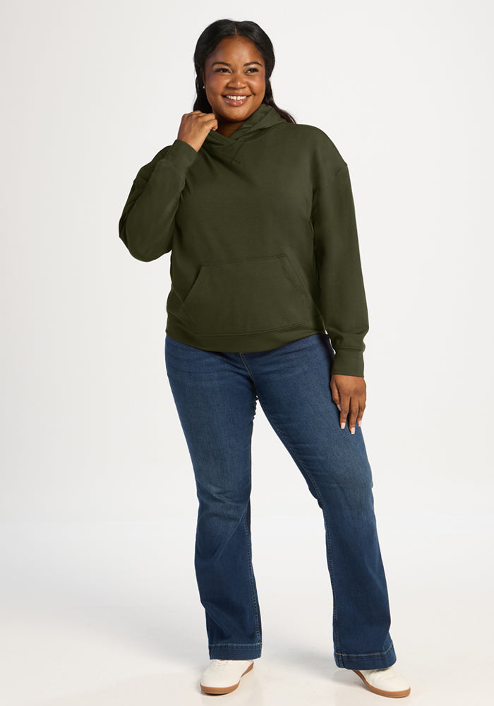 Smiling woman in Woolx Lizzy Hoodie - Everleaf and blue jeans, gently touching her hood.