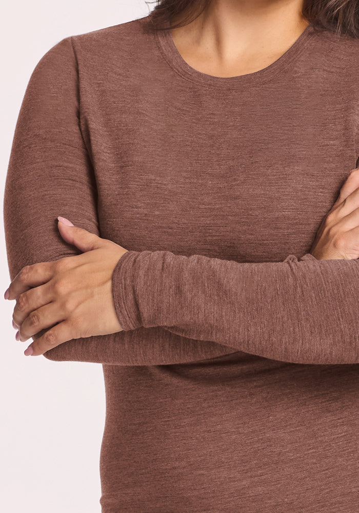 Woman in Woolx Sadie Baselayer Top - Sable Heather, long-sleeve merino wool, arms crossed, light background.
