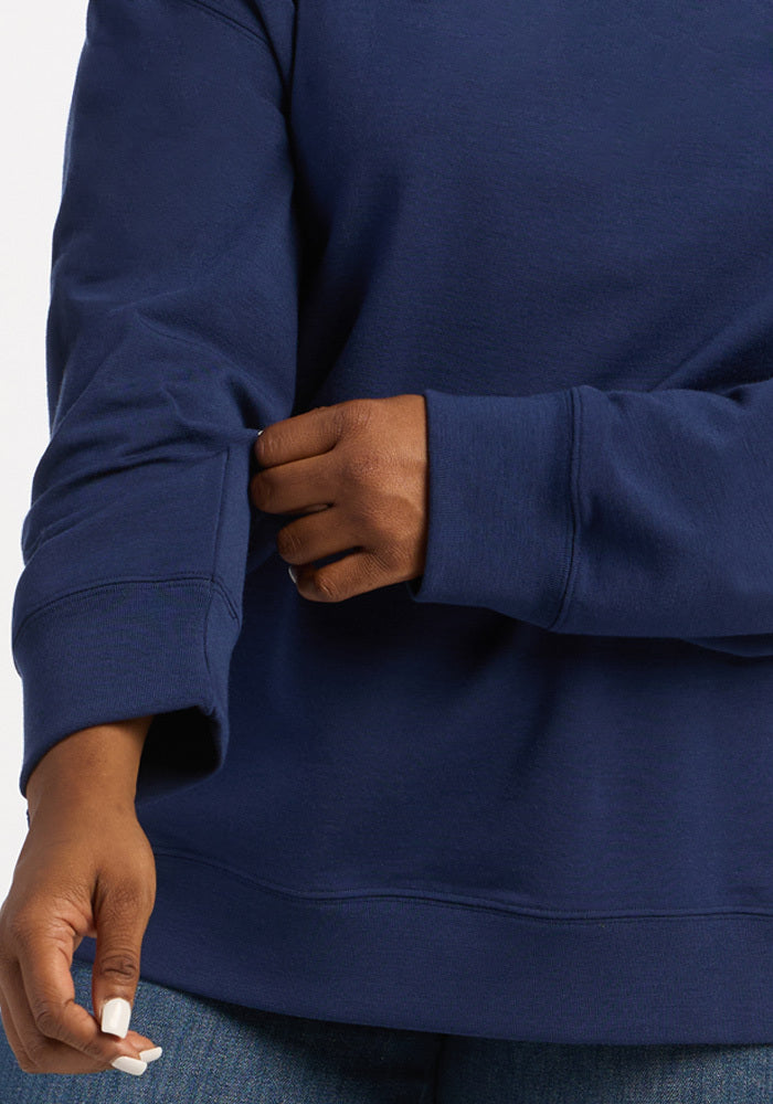 A person wearing a dark blue Woolx Genevieve Hoodie - Ocean Cavern in moisture-wicking merino wool with ribbed cuffs.
