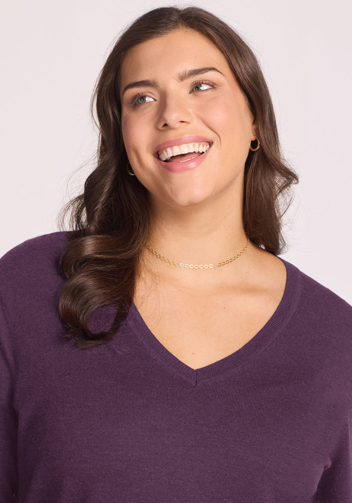 Woman with long brown hair smiles, wearing the Woolx Francesca Sweater in Purple Iris, gold hoops, and necklace.