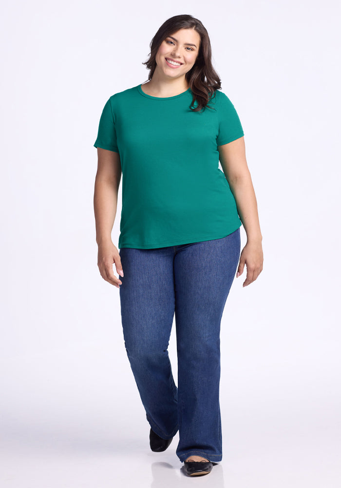 Woman smiling in a Woolx Liza Crew Neck Tee - Cabana Crush, blue jeans, and black shoes against a white background.