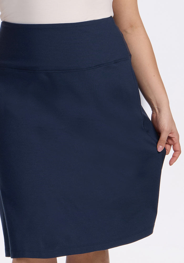A person wearing the Woolx Marilyn Flowy Midi Skirt in Deep Navy and a white top stands with one hand resting on the skirt against a plain light background.