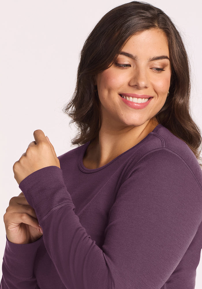 Smiling woman in a Woolx Hannah Long Sleeve Top - Purple Iris, with wavy brown hair, looking to her left.