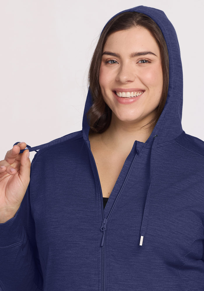 Woman smiling in the Woolx Ryann Hoodie—Twilight Storm, with hood up; a travel essential for lightweight comfort.