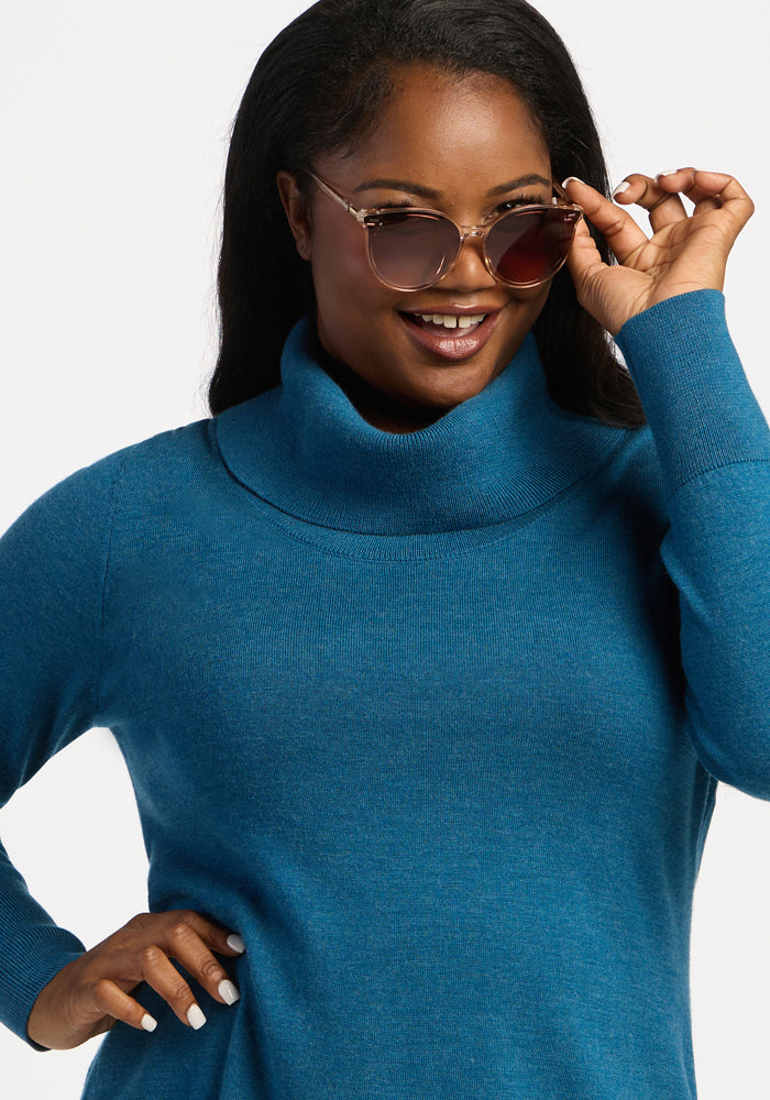 Woman in a Woolx Josie Cowl Neck Sweater - Blue Pine smiles while adjusting her sunglasses with one hand.