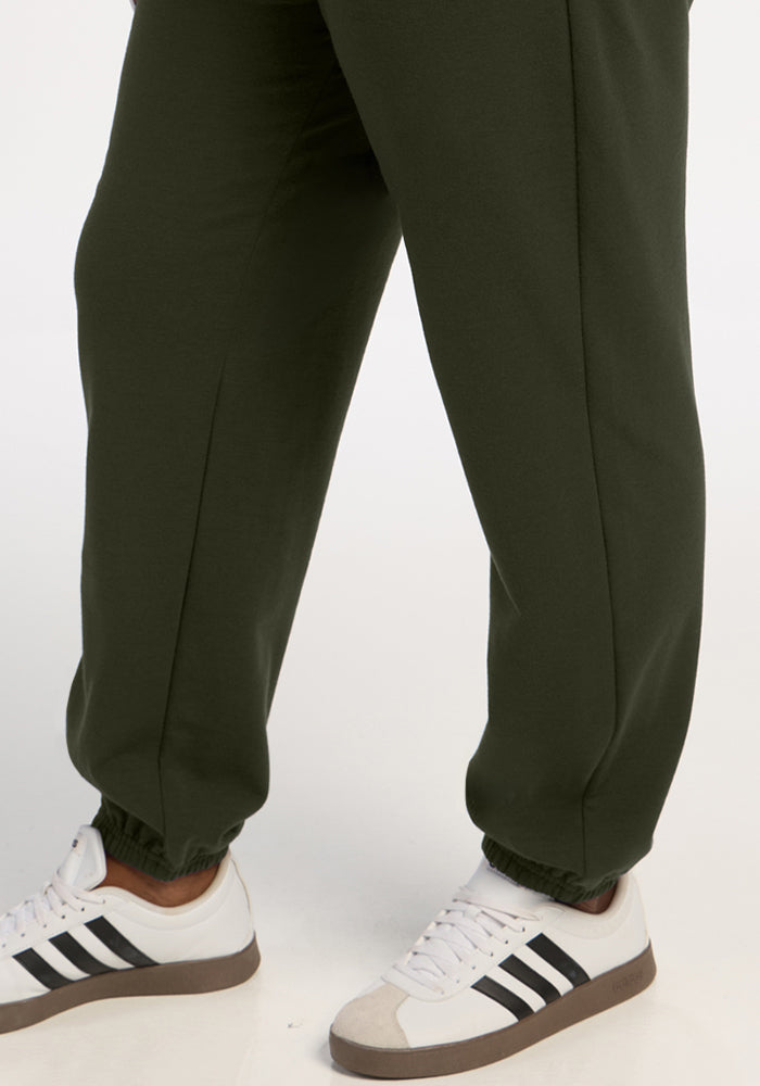 Person wearing Woolx Juliette Joggers in Duffel Bag and white Adidas sneakers with black stripes, on a white surface.