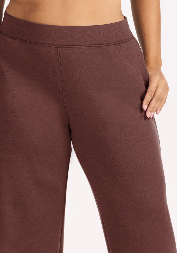 Someone in Woolx Bree Lounge Pants - Canyon Clay stands relaxed, one hand by their side, exuding laid-back style.