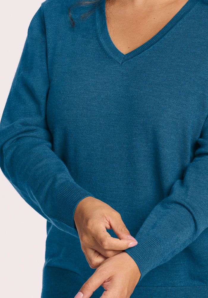 Person in a Woolx Francesca Sweater - Blue Pine, adjusting the sleeve with their right hand, light background.