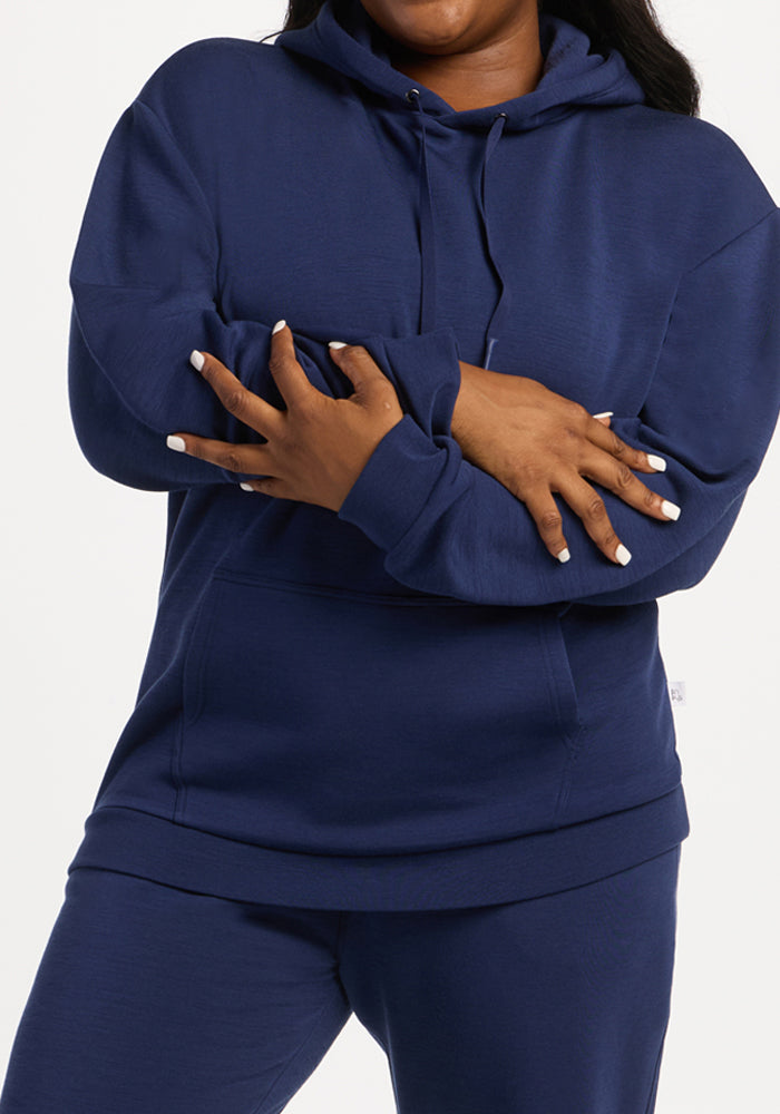 Person in a Woolx Avery Hoodie - Ocean Cavern crosses arms, displaying white nail polish against a plain backdrop.