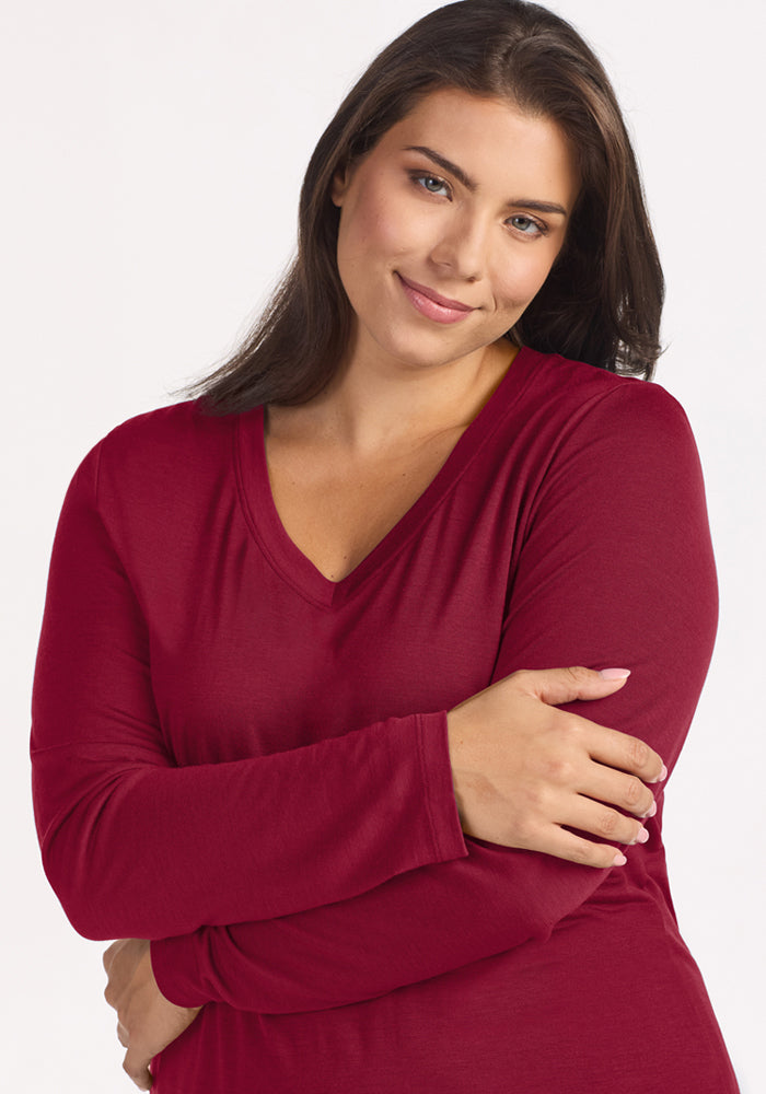 A woman with arms crossed wears a beet-red Lily V Neck Lounge Top made of Merino wool.